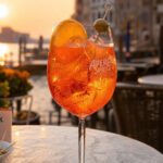 Aperol Spritz Cocktail im Glas mit Eis und Orangenscheibe auf einer Terrasse