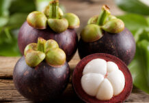 Wie schmeckt Mangostan? Aufgeschnittene Mangostan-Frucht mit weißem Fruchtfleisch auf Holztisch