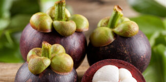 Wie schmeckt Mangostan? Aufgeschnittene Mangostan-Frucht mit weißem Fruchtfleisch auf Holztisch