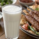 Ein Glas Ayran mit feinem Schaum neben gegrilltem Fleisch am Spieß