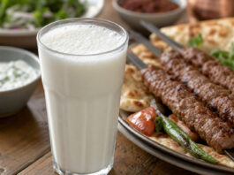 Ein Glas Ayran mit feinem Schaum neben gegrilltem Fleisch am Spieß