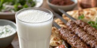 Wie schmeckt Ayran? Ein Glas Ayran mit feinem Schaum neben gegrilltem Fleisch am Spieß