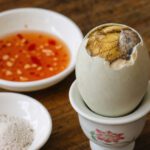 Gekochtes Balut-Ei im Eierbecher mit Salz und Chili-Dip serviert