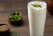 Wie schmeckt Buttermilch? Ein Glas gekühlte Buttermilch mit Kondenswasser auf einem Holztisch