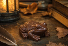 Chocolate Frog – Wie schmeckt der Schokofrosch aus Harry Potter? Froschförmige Schokolade auf einem alten Holzschreibtisch, Symbolbild für den Chocolate Frog aus Harry Potter
