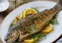 Wie schmeckt Forelle? Gegrillte Forelle auf einem Teller mit Zitrone und Kräutern