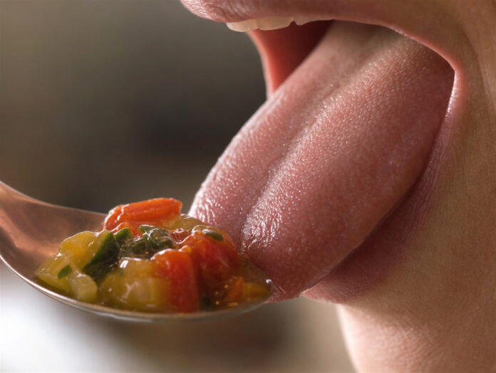 Nahaufnahme einer Zunge beim Schmecken Nahaufnahme einer Zunge beim Schmecken eines Löffels Essen