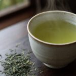 Tasse grüner Tee mit losen Teeblättern auf Holztisch