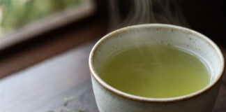Wie schmeckt grüner Tee? Tasse grüner Tee mit losen Teeblättern auf Holztisch