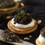 Kaviar auf Blini mit Crème fraîche, serviert mit einem Perlmuttlöffel