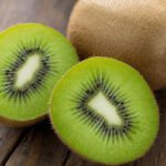 Aufgeschnittene Kiwi mit saftig-grünem Fruchtfleisch und schwarzen Kernen neben einer ganzen Kiwi