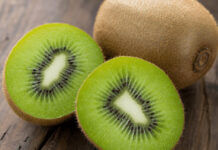 Wie schmeckt Kiwi? Aufgeschnittene Kiwi mit saftig-grünem Fruchtfleisch und schwarzen Kernen neben einer ganzen Kiwi