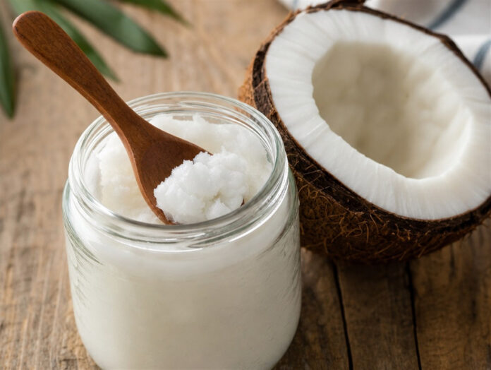 Kokosöl im Glas mit Kokosnuss Glas mit festem Kokosöl neben einer halbierten Kokosnuss