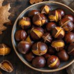 Geröstete Maronen mit aufgeschnittener Schale in einer Schüssel auf einem Holztisch, herbstliche Stimmung