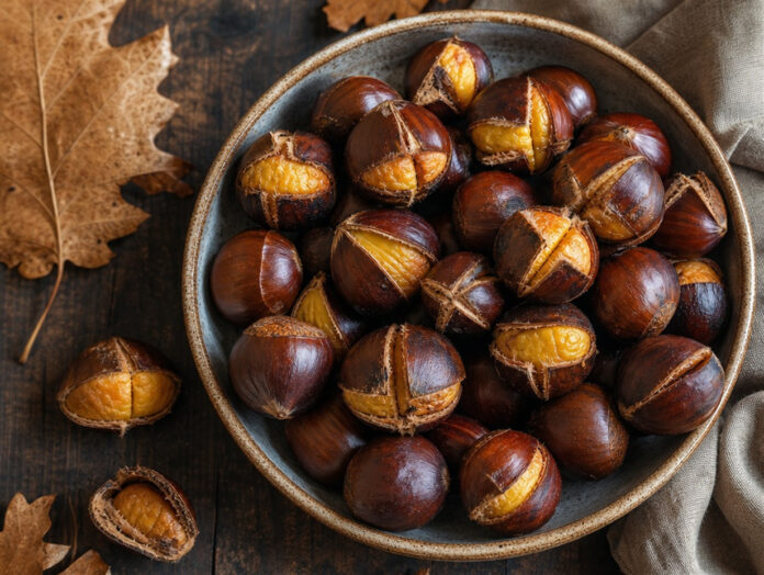 Geröstete Maronen in Schale Geröstete Maronen mit aufgeschnittener Schale in einer Schüssel auf einem Holztisch, herbstliche Stimmung