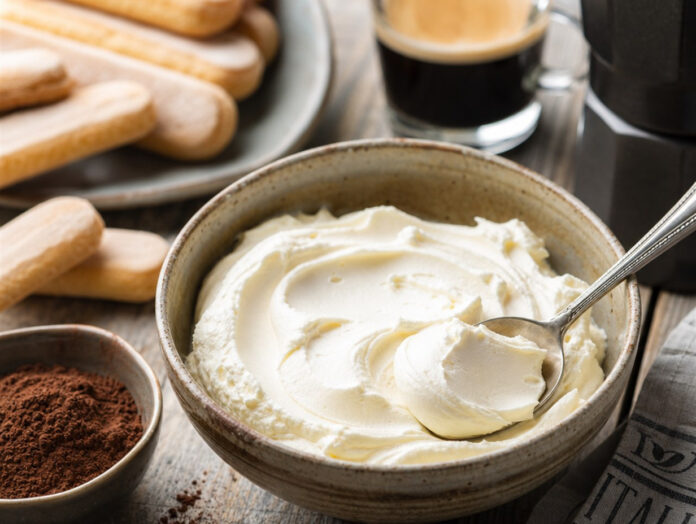 Mascarpone in einer Schale mit Löffel Cremiger Mascarpone in einer Schale mit Löffel neben Tiramisu-Zutaten