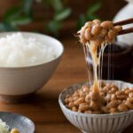 Eine Schale Natto mit klebrigen Fäden, angehoben mit Stäbchen
