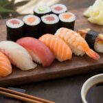 Nigiri und Maki Sushi auf dunklem Holzbrett mit Stäbchen und Ingwer