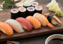 Woher kommt Sushi ursprünglich? Nigiri und Maki Sushi auf dunklem Holzbrett mit Stäbchen und Ingwer