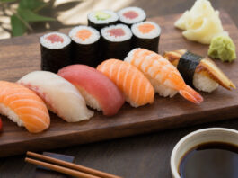 Woher kommt Sushi ursprünglich? Nigiri und Maki Sushi auf dunklem Holzbrett mit Stäbchen und Ingwer
