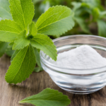 Frische grüne Stevia-Blätter neben einer Schale mit weißem Stevia-Süßstoffpulver