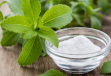 Wie schmeckt Stevia? Frische grüne Stevia-Blätter neben einer Schale mit weißem Stevia-Süßstoffpulver