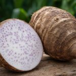 Eine halbierte Taro-Knolle mit violett gesprenkeltem Fruchtfleisch neben einer ganzen Taro-Knolle