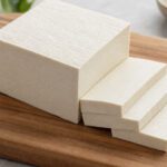 Ein Block Tofu teilweise in Scheiben geschnitten auf einem Schneidebrett