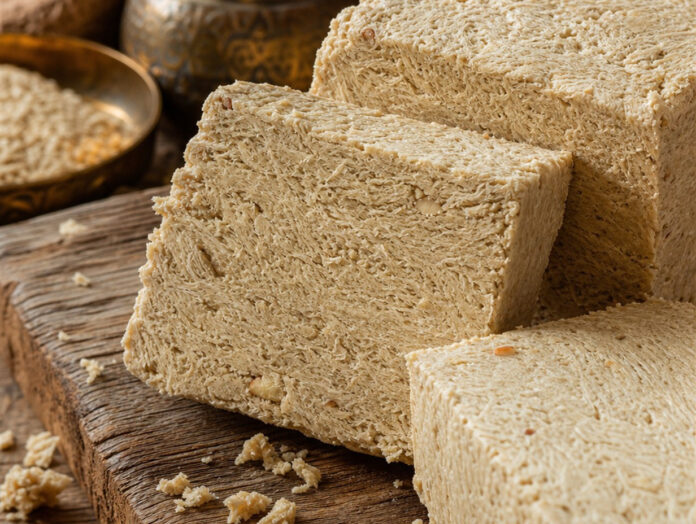 Halva – orientalische Süßspeise aus Sesam Aufgeschnittene Halva mit sichtbarer krümeliger Sesamstruktur auf Holzuntergrund