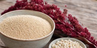 Wie schmeckt Amaranth? Große Schale mit winzigen hellen Amaranthkörnern neben einer kleinen Schale gepopptem Amaranth und roten Amaranthblütenrispen