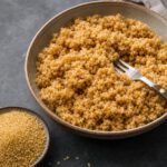 Schale mit gekochtem goldbraunem Bulgur mit deutlich erkennbaren einzelnen Körnern, daneben roher Bulgur