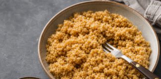 Wie schmeckt Bulgur? Schale mit gekochtem goldbraunem Bulgur mit deutlich erkennbaren einzelnen Körnern, daneben roher Bulgur