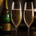 Zwei hohe Champagnergläser mit blassgoldenem Schaumwein und feiner aufsteigender Perlenschnur auf dunklem Tisch