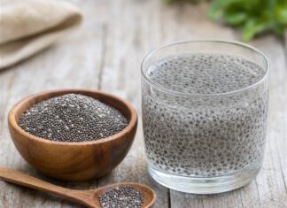 Wie schmecken Chiasamen? Holzschale mit trockenen dunklen Chiasamen neben einem Glas Wasser, in dem die Samen zu durchsichtigem Gel aufgequollen sind