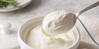 Wie schmeckt Crème fraîche? Weißes Keramiktöpfchen mit dicker glänzender Crème fraîche, ein Löffel hebt eine standfeste Portion heraus