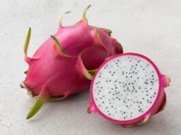 Ganze pinke Drachenfrucht mit grünen Schuppen neben einer aufgeschnittenen Hälfte mit weißem Fruchtfleisch