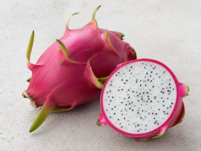 Ganze pinke Drachenfrucht mit grünen Schuppen neben einer aufgeschnittenen Hälfte mit weißem Fruchtfleisch