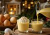 Was ist Eierlikör? Zwei Gläser mit dickflüssigem gelbem Eierlikör, in eines wird aus einer Karaffe nachgeschenkt, daneben braune Eier in einer Schale