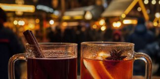 Glühwein oder Punsch: Was ist der Unterschied? Zwei Glasbecher nebeneinander auf einem Holztisch, links dunkelroter Glühwein mit Zimtstange, rechts orangeroter Fruchtpunsch mit Apfel- und Orangenscheiben und Sternanis