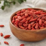 Getrocknete orangerote Goji-Beeren mit runzliger Oberfläche in einer Holzschale auf hellem Stein