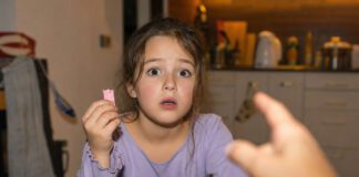 Was passiert, wenn man Kaugummi verschluckt? Kind sitzt erschrocken am Küchentisch und hält einen angebissenen Kaugummistreifen