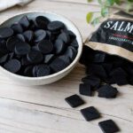 Tiefschwarze Lakritzpastillen und Rauten in einer Schale auf hellem Holz