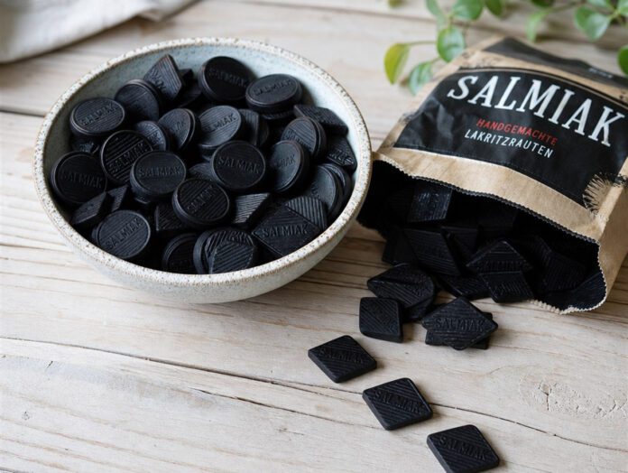 Tiefschwarze Lakritzpastillen und Rauten in einer Schale auf hellem Holz