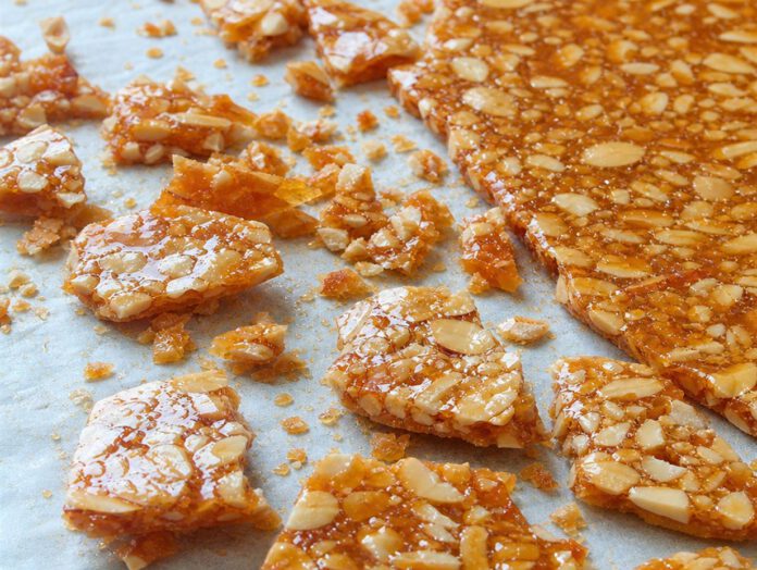 Grob gebrochene Stücke goldbrauner Mandelkrokant auf hellem Backpapier, daneben eine noch ganze erstarrte Krokantplatte