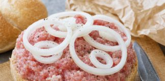 Welt-Mettbrötchen-Tag: Warum rohes Mett so streng geregelt ist Halbes Brötchen dick mit rohem gewürztem Mett belegt, darauf rohe Zwiebelringe und grober Pfeffer