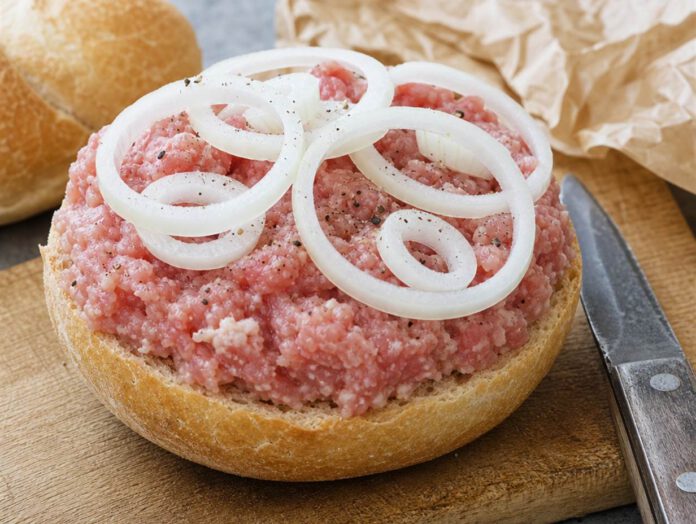Halbes Brötchen dick mit rohem gewürztem Mett belegt, darauf rohe Zwiebelringe und grober Pfeffer