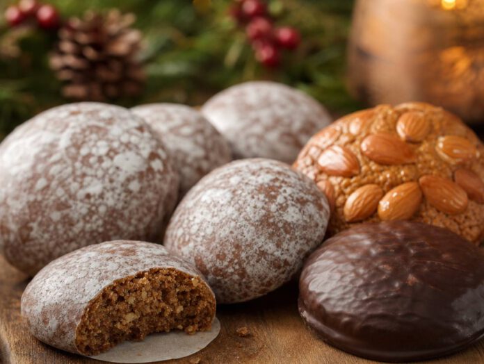 Mehrere runde Oblatenlebkuchen mit Zuckerglasur, Schokoladenüberzug und Mandelbelag, einer angebrochen mit sichtbarer nussiger Masse