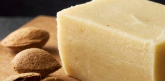 Was ist Persipan? Heller Block Persipanrohmasse auf einem Holzbrett, davor aufgebrochene Steine mit mandelähnlichen Kernen