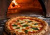 Tag der Pizza am 9. Februar: Termine, Spezifikation und Belag Neapolitanische Margherita auf einem Holzschieber mit luftigem Rand und dunklen Blasen vor der Öffnung eines Holzofens