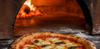 Tag der Pizza am 9. Februar: Termine, Spezifikation und Belag Neapolitanische Margherita auf einem Holzschieber mit luftigem Rand und dunklen Blasen vor der Öffnung eines Holzofens